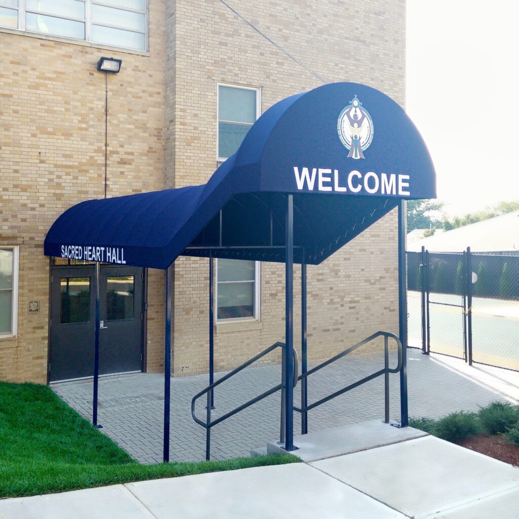 Fabric-covered walkway canopy for school entrance, featuring curved design and white lettering for Sacred Heart Hall building, designed and installed by Window Works NJ