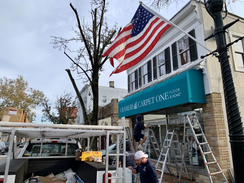 Installation of custom teal Sunbrella® commercial awning at Cramers Carpet One storefront in Madison, NJ, by Window Works New Jersey.