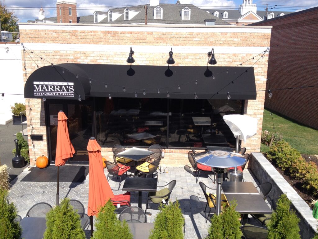 Modern black fabric awning over storefront and outdoor dining setup with patio furniture, umbrellas, and string lights at Marra’s Restaurant, Livingston NJ.